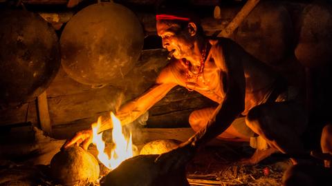 Ein Mann macht auf einer Feuerstelle aus Steinen ein Feuer zum kochen. 