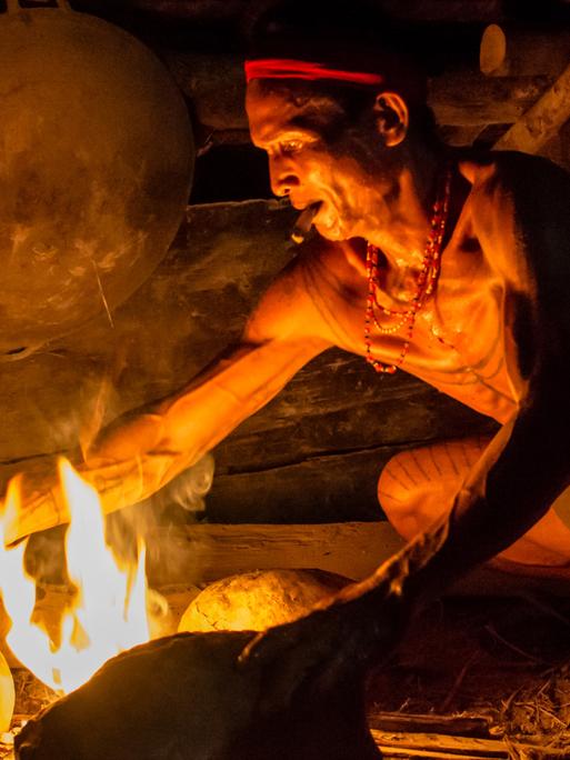 Ein Mann macht auf einer Feuerstelle aus Steinen ein Feuer zum kochen. 