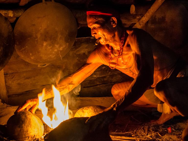 Ein Mann macht auf einer Feuerstelle aus Steinen ein Feuer zum kochen. 