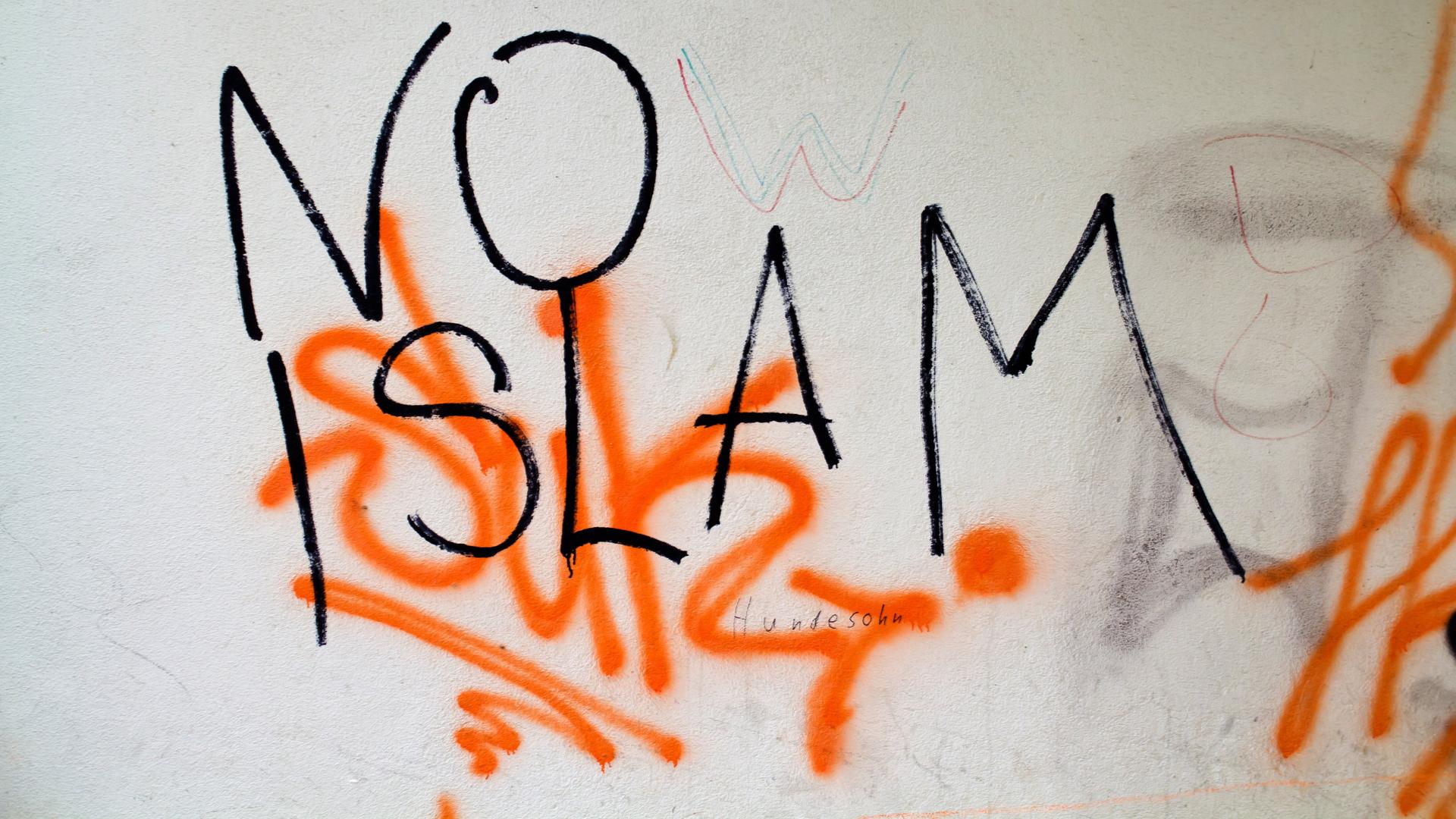 An einer Mauer steht in schwarzer Schrift "No Islam" und Gekritzel in orange. An einer Mauer steht in schwarzer Schrift "No Islam" und Gekritzel in orange.