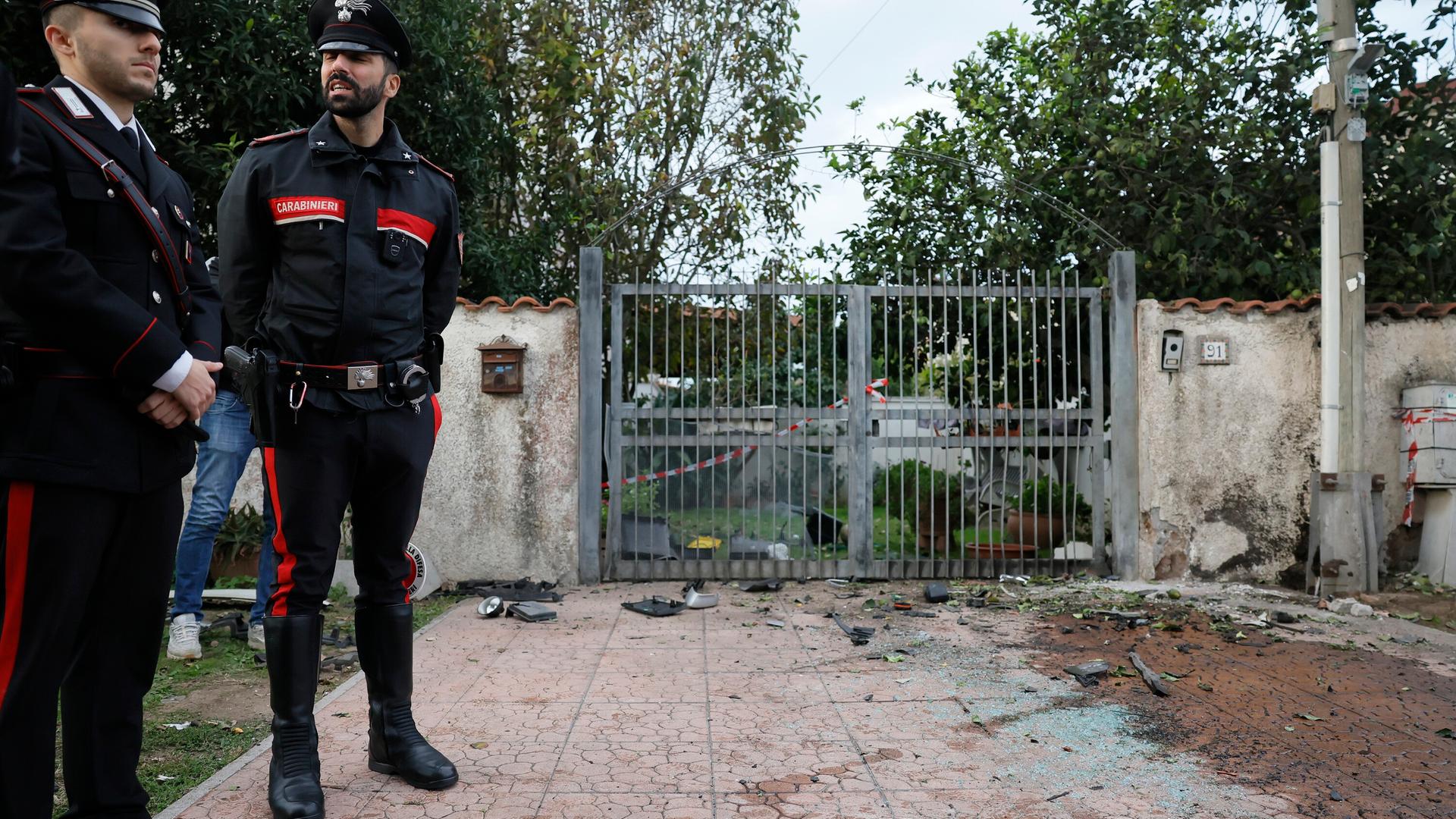 Zwei Polizisten stehen vor dem Zaun des Hauses von Sigfrido Ranucci. Links sieht man die Spuren der Explosion.