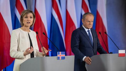 Das Bild zeigt Kristrun Frostadottir und Donald Tusk nebeneinader an Redepulten mit Mikrofonen. Im Hintergrund sind mehrere isländische und polnische Flaggen zu sehen.