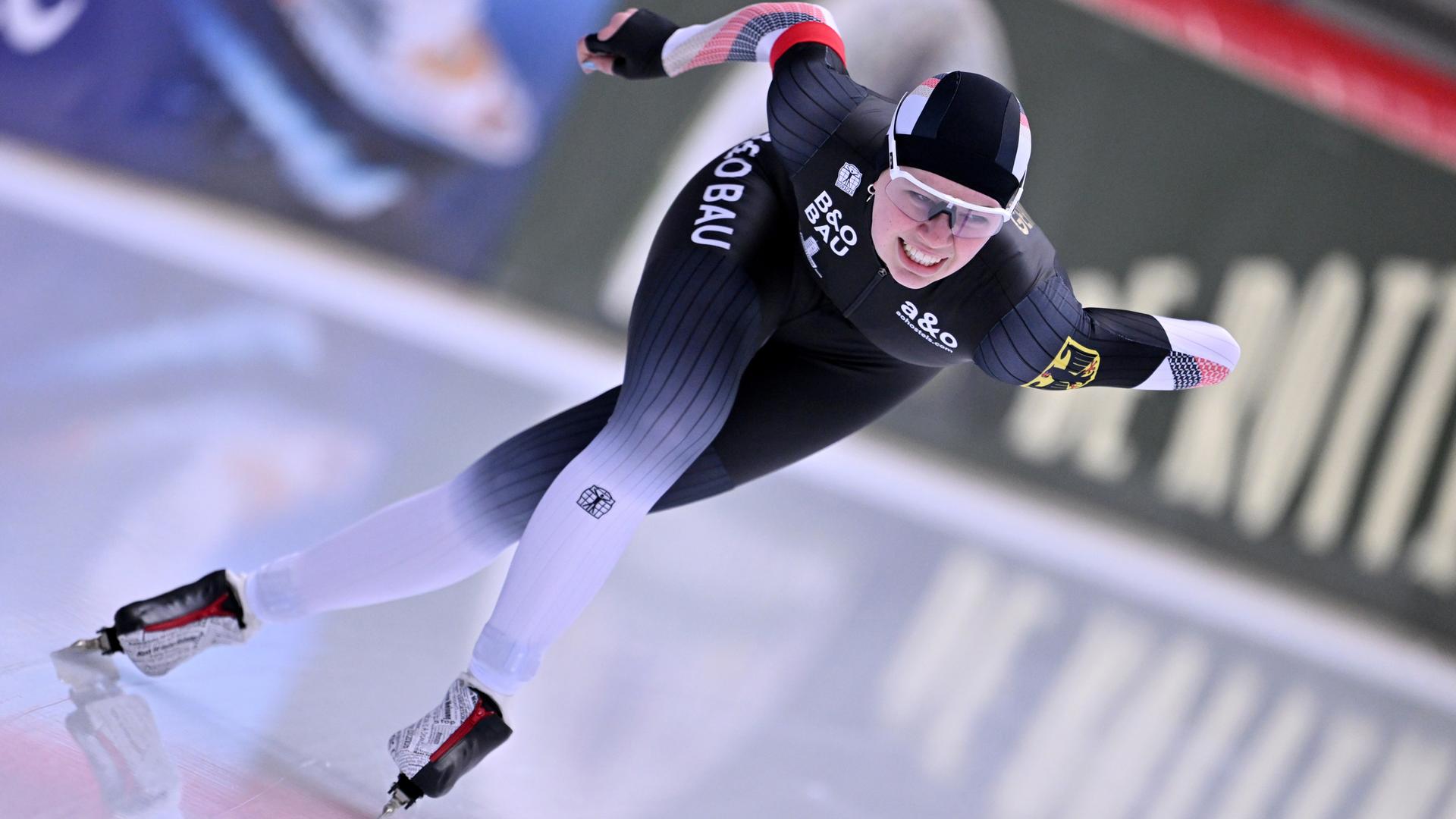 Das Bild zeigt die deutsche Eisschnelläuferin Josephine Schlörb in Aktion auf der Eispiste. Sie trägt einen für diese Sportart typischen, hautengen Ganzkörperanzug mit Kapuze für die Haare.