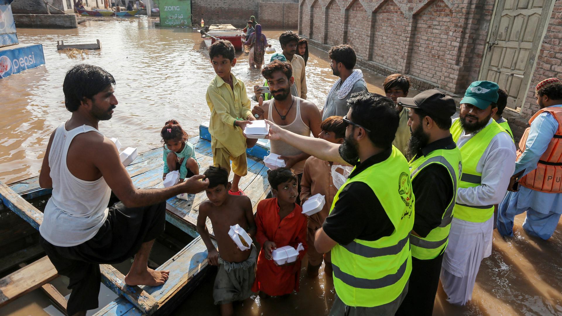 Freiwillige Helfer verteilen Lebensmittel an die pakistanische Bevölkerung. Im Hintergrund sind die Ausmaße der Überschwemmungen zu sehen. Freiwillige Helfer verteilen Lebensmittel an die pakistanische Bevölkerung. Im Hintergrund sind die Ausmaße der Überschwemmungen zu sehen.