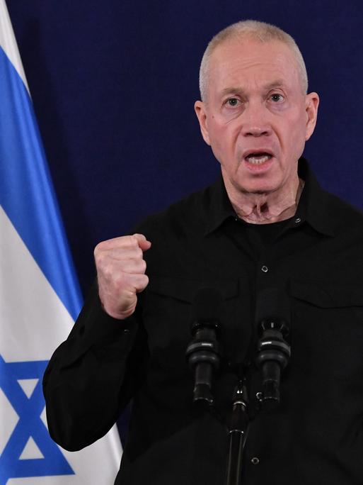 Israels Verteidigunngsminister Minister Joaw Galant steht mit geballter Faust vor einem Mikrofon, hinter ihm eine Israel-Flagge.