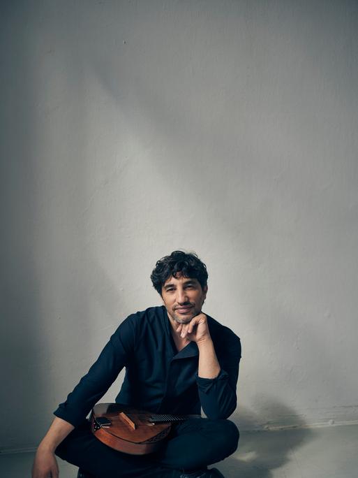 Avi Avital sitzt im Schneidersitz vor der Kamera und lächelt, während seine Mandoline im Schoß liegt.