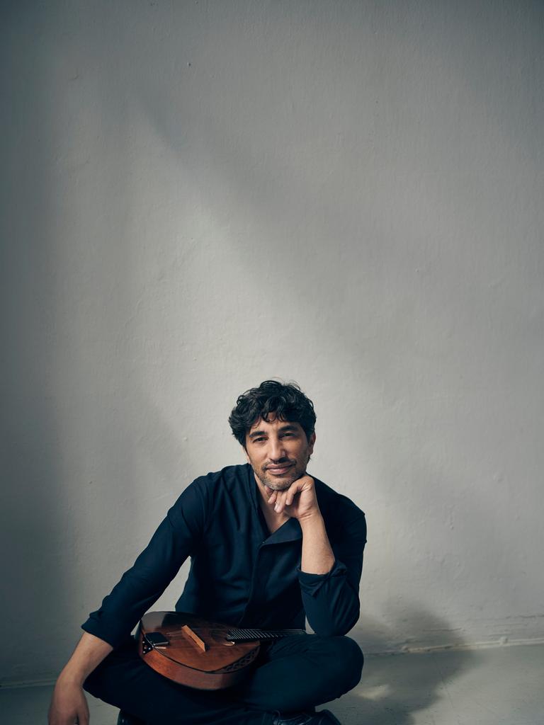 Avi Avital sitzt im Schneidersitz vor der Kamera und lächelt, während seine Mandoline im Schoß liegt.
