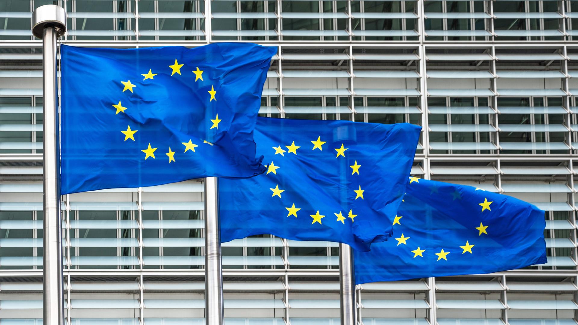 Drei blaue Europaflaggen wehen vor dem Sitz der Europäischen Kommission. 