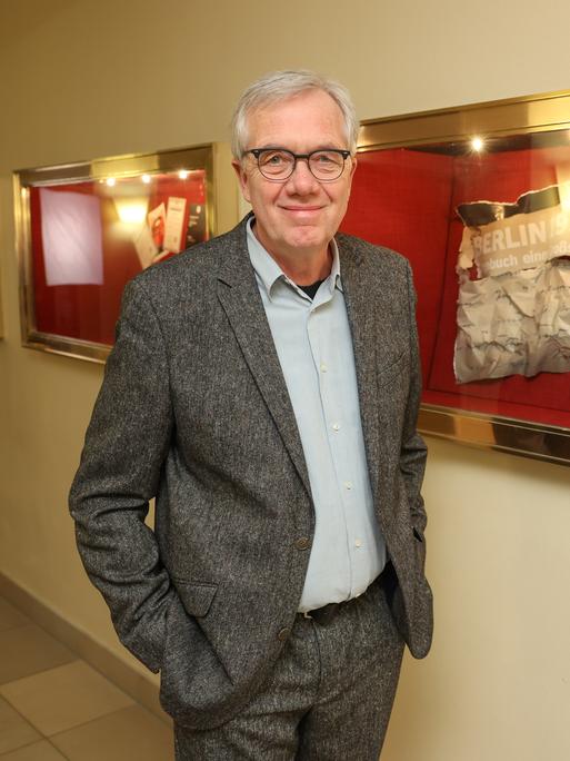 Volker Heise steht im Eingang eines Kinos vor den Aushangtafeln. Er trägt einen grauen Anzug und lächelt in die Kamera.