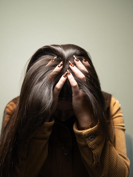 Eine Frau trauert und verbirgt ihr Gesicht hinter Haaren und Händen.