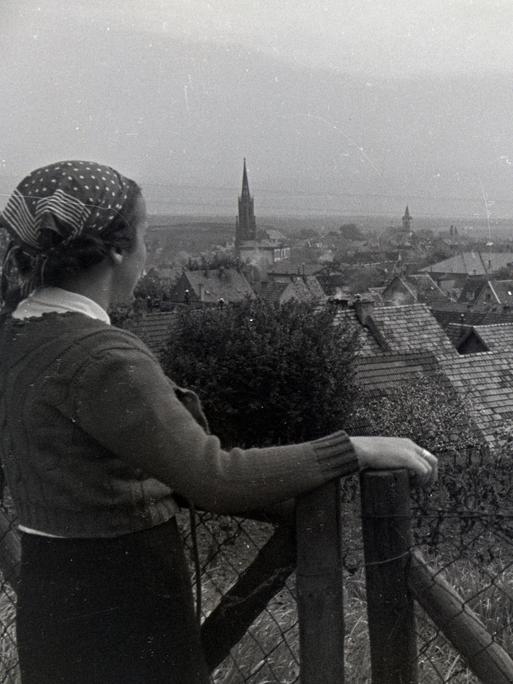 Schwarzweißaufnahme einer Frau mit Kopftuch, die auf ein Dorf in der Pfalz schaut.