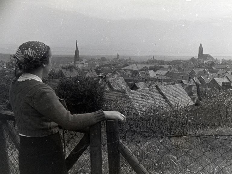 Schwarzweißaufnahme einer Frau mit Kopftuch, die auf ein Dorf in der Pfalz schaut.