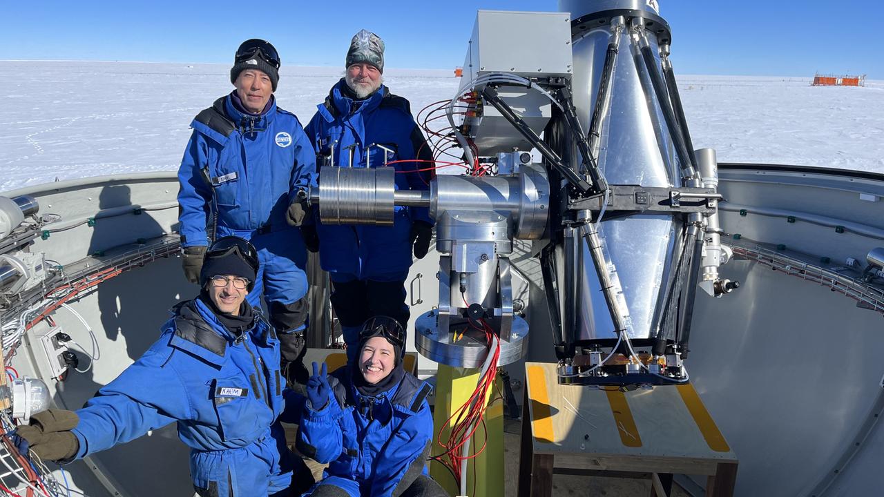 Wissenschaftler sitzen in blauen Schutzanzügen vor einem Weltraumteleskop Mitten im Eis