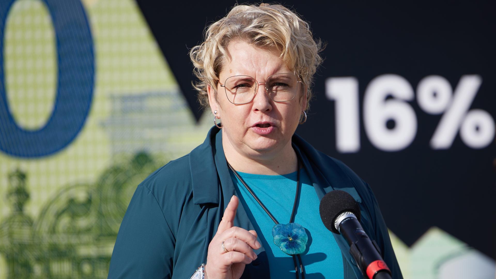 Maike Finnern, GEW-Vorsitzende, steht vor einem Mikrofon und hebt den Zeigefinger der rechten Hand.