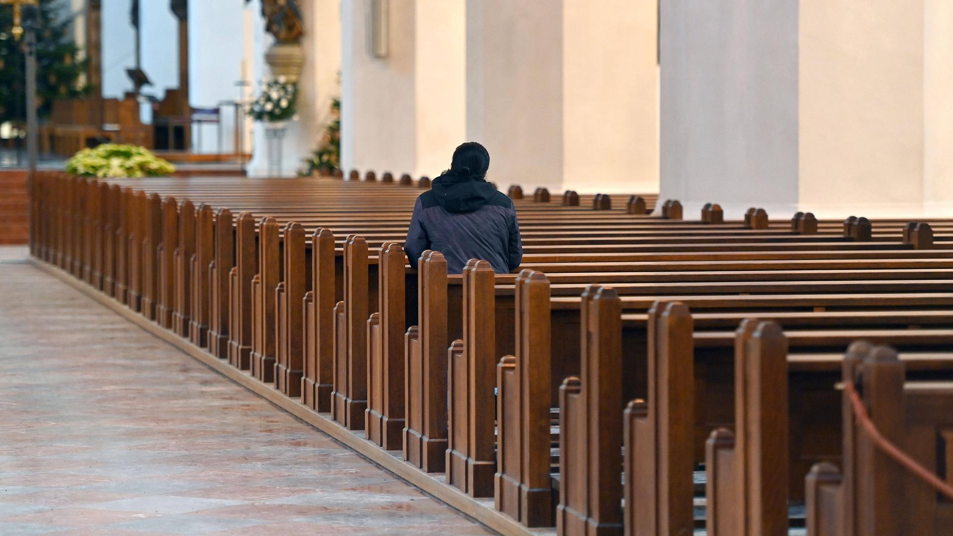 Ein einzelner Mann sitzt auf einer Kirchenbank in ansonsten leeren Sitzreihen.