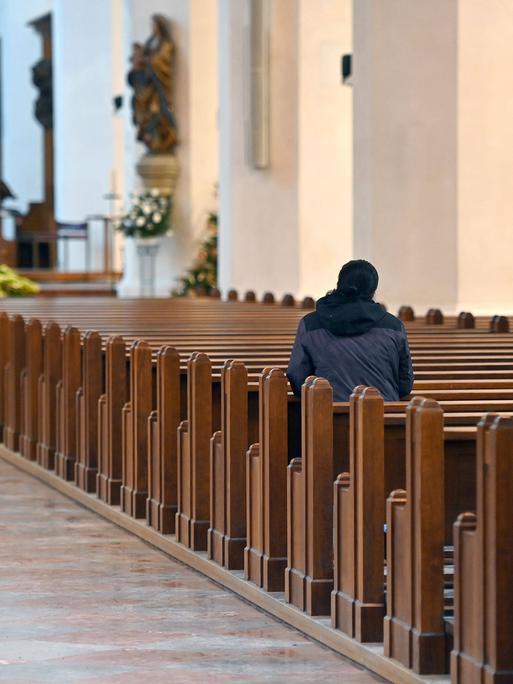 Ein einzelner Mann sitzt auf einer Kirchenbank in ansonsten leeren Sitzreihen.