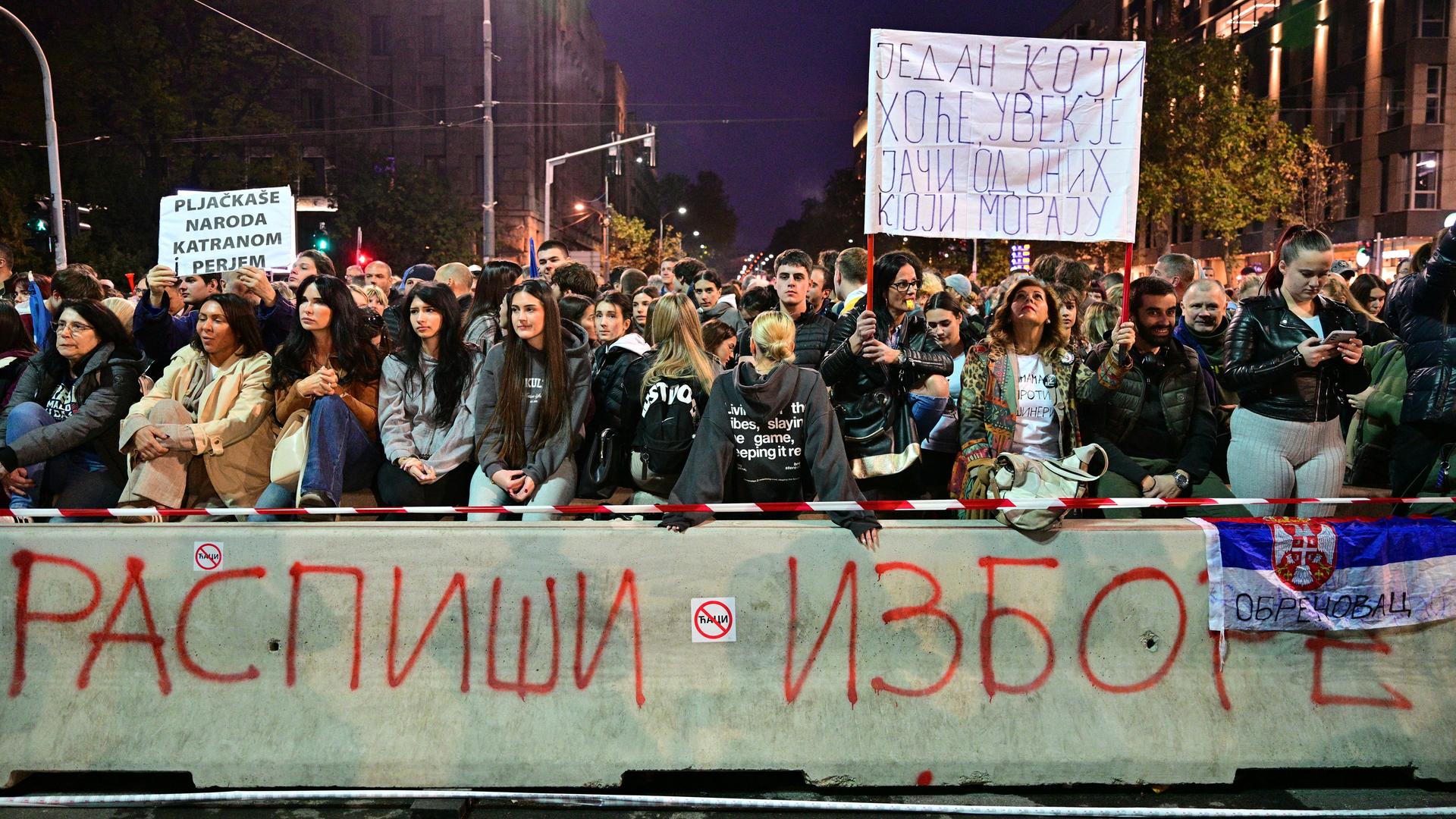 Studenten und andere Regierungskritiker bei erneuten Protesten in Belgrad gegen die serbische Regierung. Eine Frau hebt ein Schild mit einer blutigen Hand hoch. 