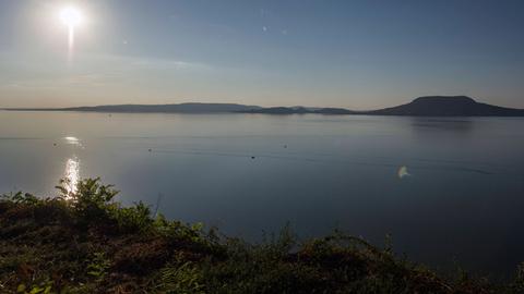 Das Bild blickt von der südlichen Seite auf den Plattensee. Der Himmel ist blau, anhand des Sonnenstandes kann man vom späten Nachmittag im Sommer ausgehen. 