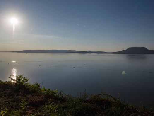 Das Bild blickt von der südlichen Seite auf den Plattensee. Der Himmel ist blau, anhand des Sonnenstandes kann man vom späten Nachmittag im Sommer ausgehen. 