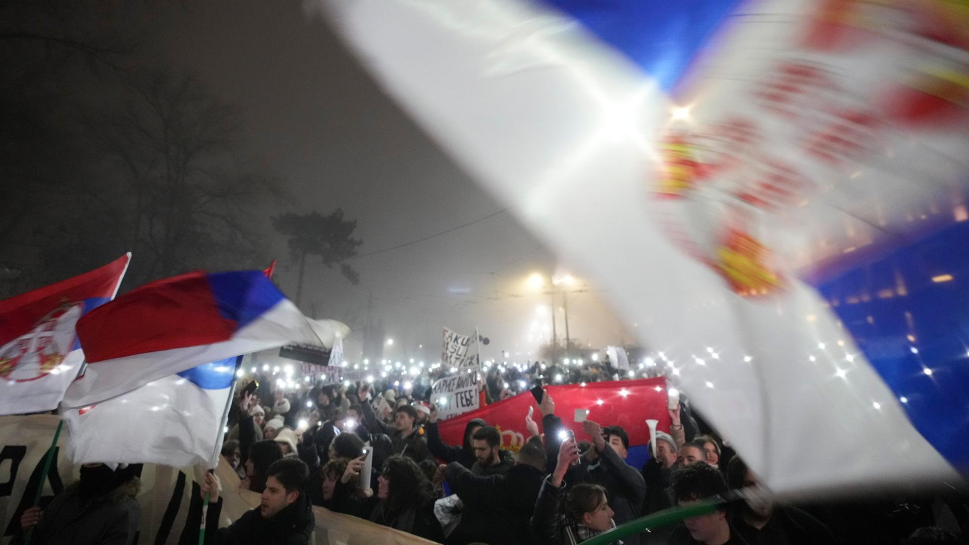 Tausende Studierende marschieren am Silvesterabend in Belgrad. Sie schwenken serbische Fahnen und halten Plakate hoch. Viele haben außerdem die Taschenlampen ihrer Smartphones eingeschaltet.