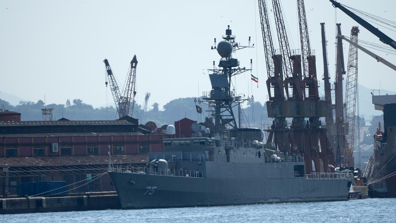 Das Bild zeigt ein Kriegsschiff, das in einem Hafen liegt. Im Hintergrund sind Kräne zu sehen.