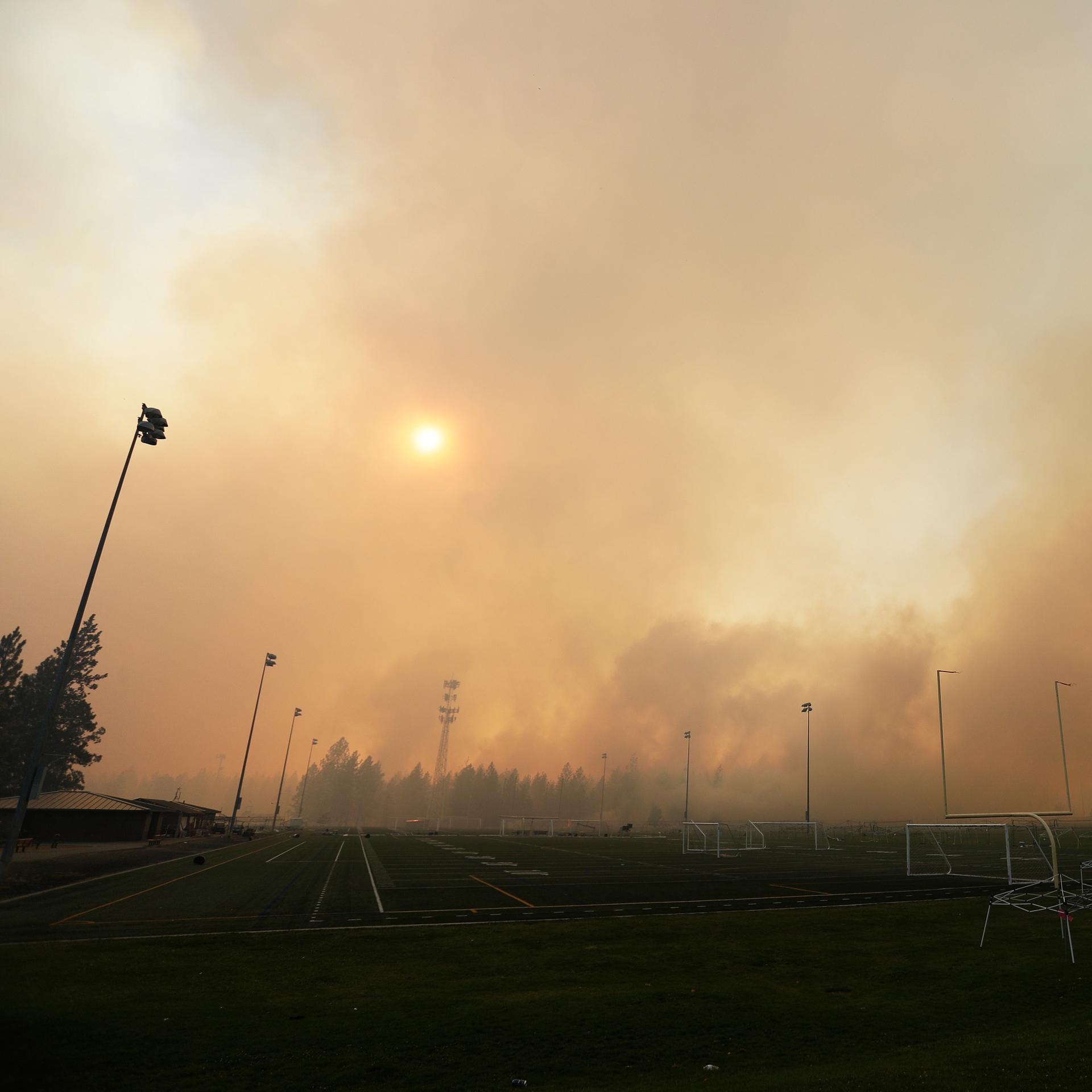 Qualm und Rauch von einem Brand an einer Straße. Die Sonne ist durch den Schleier kaum noch zu sehen.