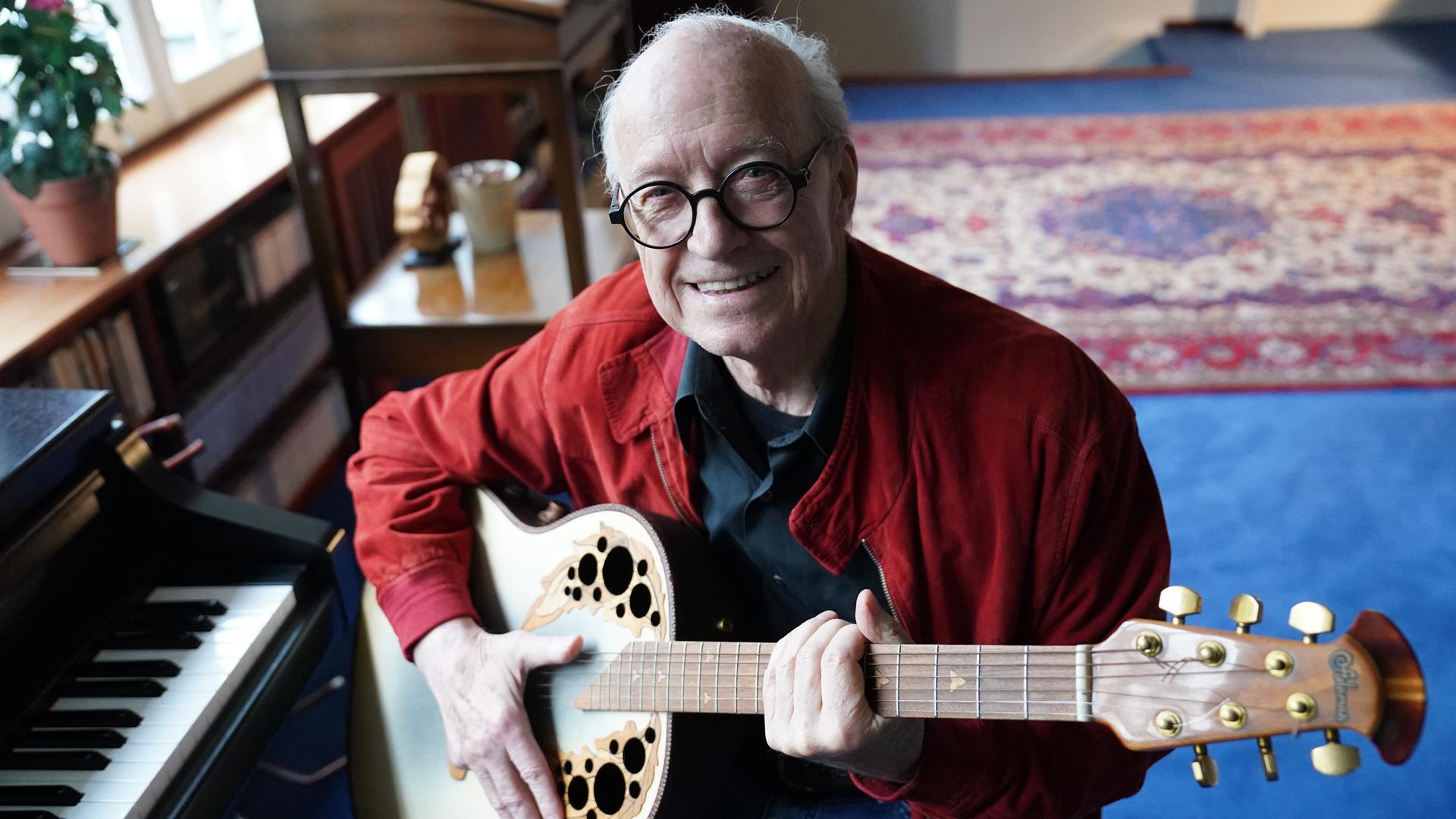 Michael Kunze, Liedermacher und Komponist, sitzt mit seiner Gitarre in seinem Arbeitszimmer. 
