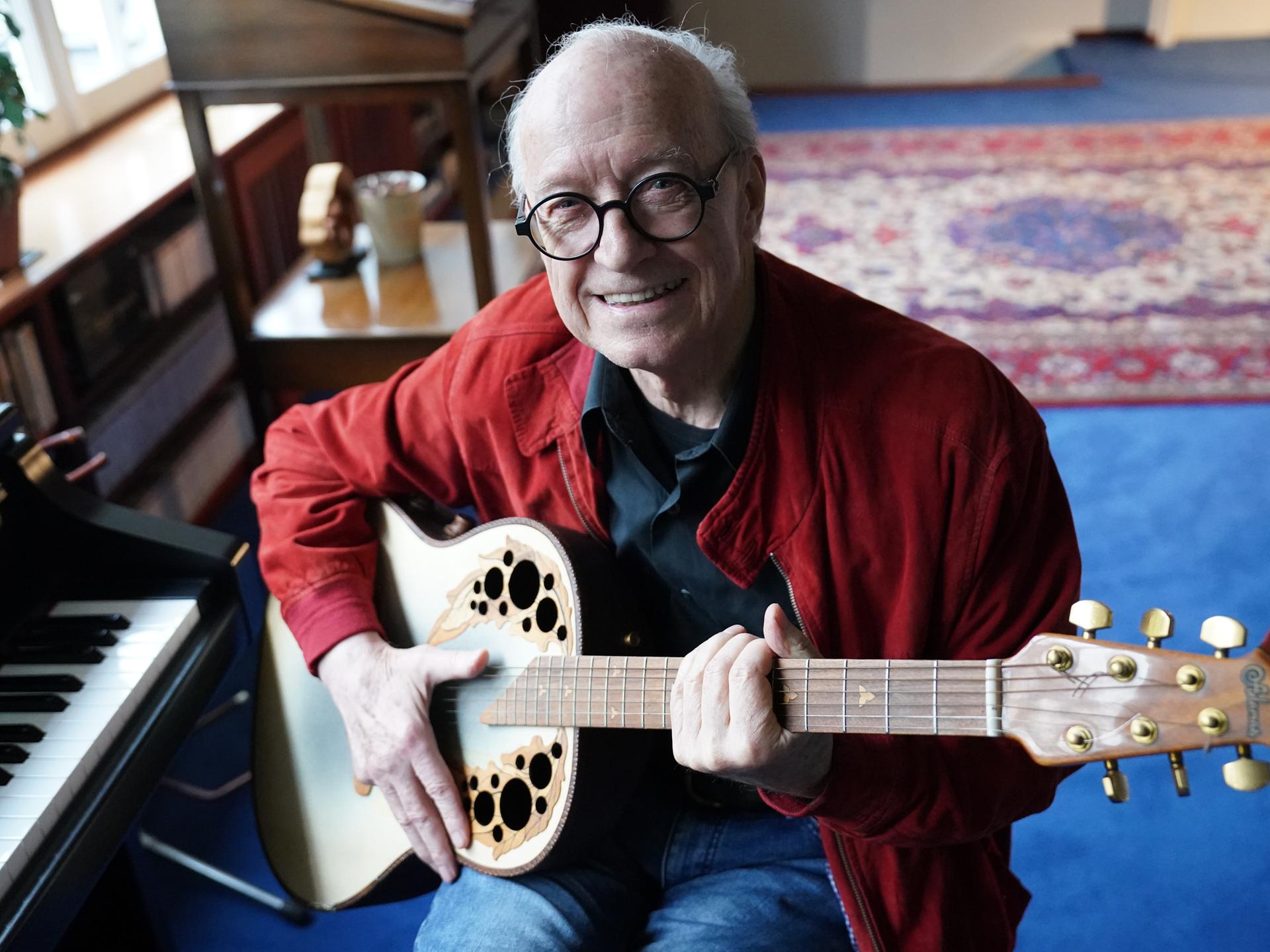 Michael Kunze, Liedermacher und Komponist, sitzt mit seiner Gitarre in seinem Arbeitszimmer. 