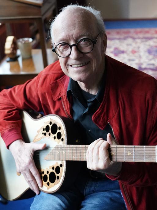 Michael Kunze, Liedermacher und Komponist, sitzt mit seiner Gitarre in seinem Arbeitszimmer. 