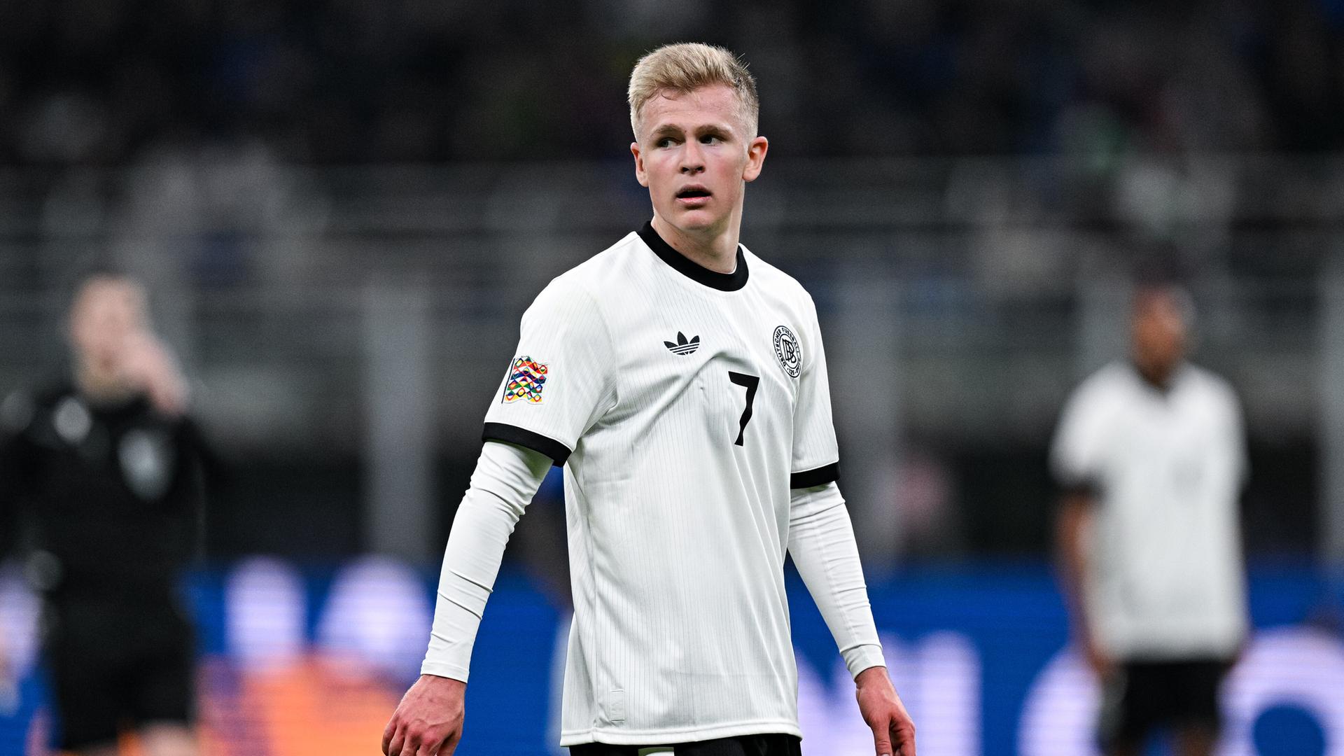 Jonathan Burkardt trägt ein schwarz-weißes Trikot der deutschen Nationalmannschaft und steht auf dem Speilfeld. Er schaut angestrengt zur Seite. Jonathan Burkardt trägt ein schwarz-weißes Trikot der deutschen Nationalmannschaft und steht auf dem Speilfeld. Er schaut angestrengt zur Seite.