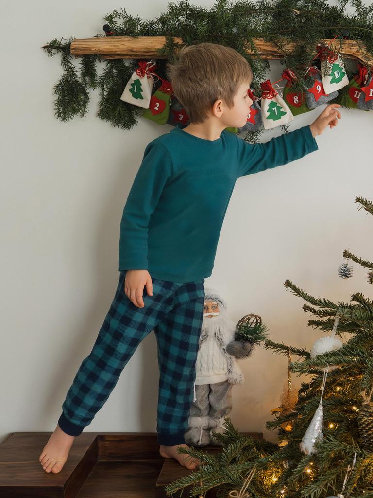 Ein Junge greift nach einem Säckchen im Adventskalender, neben ihm steht ein kleiner geschmückter Weihnachtsbaum