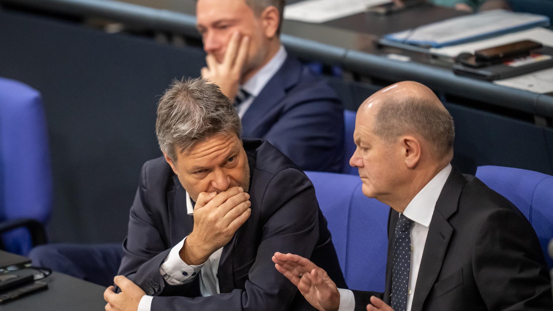 Koalitionsspitzen im Bundestag: Wirtschafts- und Klimaschutzminister Robert Habeck (M., Grüne) redet mit vorgehaltener Hand mit Bundeskanzler Olaf Scholz (r., SPD). Im Hintergrund ist unscharf Finanzminister Christian Lindner (FDP) zu sehen.