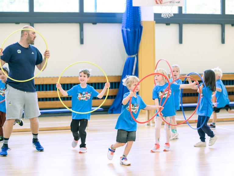 Ein Trainer zeigt den Kindern Übungen mit dem Hula-Hoop-Reifen.