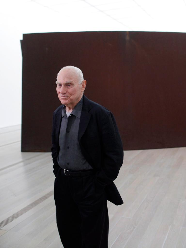 Der Künstler Richard Serra steht vor einer Stahlskulptur.