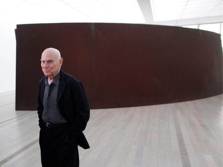 Der Künstler Richard Serra steht vor einer Stahlskulptur.
