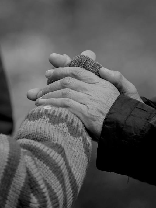 Pflegende Hände: Schwarz-Weiß-Bild von zwei Händen, die die Hand einer anderen Person halten.