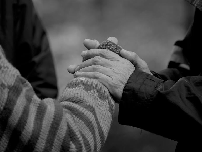Pflegende Hände: Schwarz-Weiß-Bild von zwei Händen, die die Hand einer anderen Person halten.