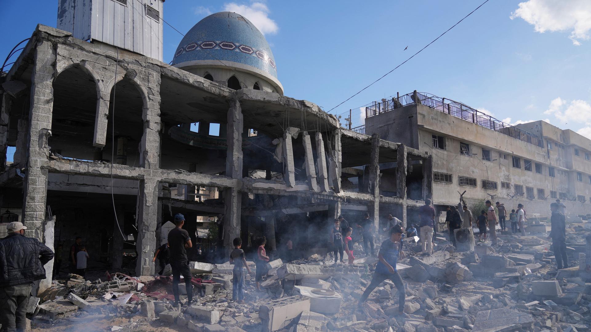 Vor der zerbombten Al-Ansar Mosque im Gaza-Streifen laufen mehrere Menschen zwischen Trümmern herum.