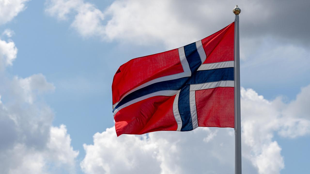 Die norwegische Nationalflagge weht im Wind vor einem blauen Himmel mit einige Wolken. 