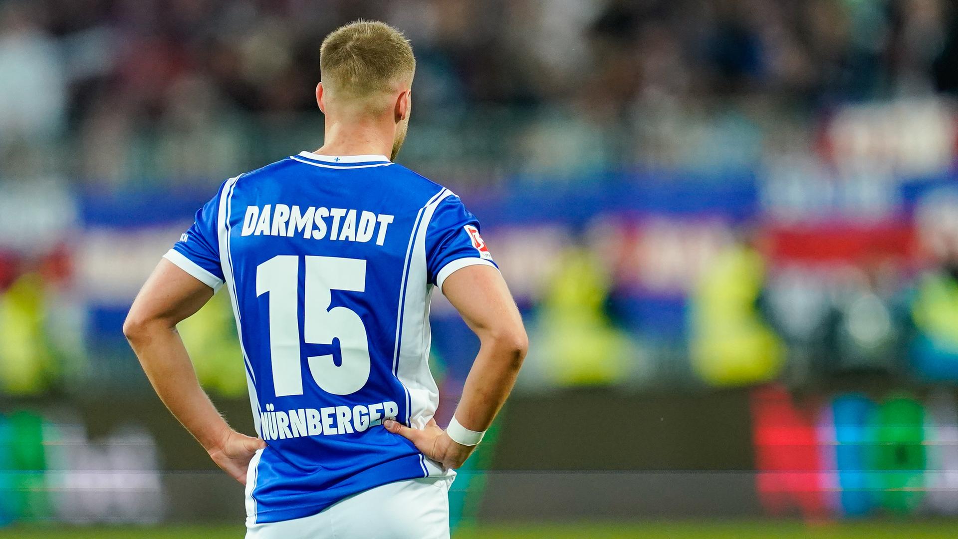 Darmstadts Fabian Nürnberger steht auf dem Spielfeld, er ist von hinten zu sehen, wie er die Arme in die Seiten stemmt.