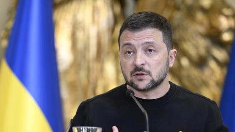 Der ukrainische Präsident Wolodymyr Selenskyj an einem Rednerpult. Im Hintergrund sieht man zwei Flaggen.
