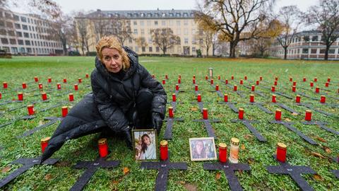 Inka Orth stellt auf einer Wiese, auf der mehrere schwarze Kreuze liegen, das Porträt ihrer verstorbenen Tochter Johanna neben eine Kerze ab.