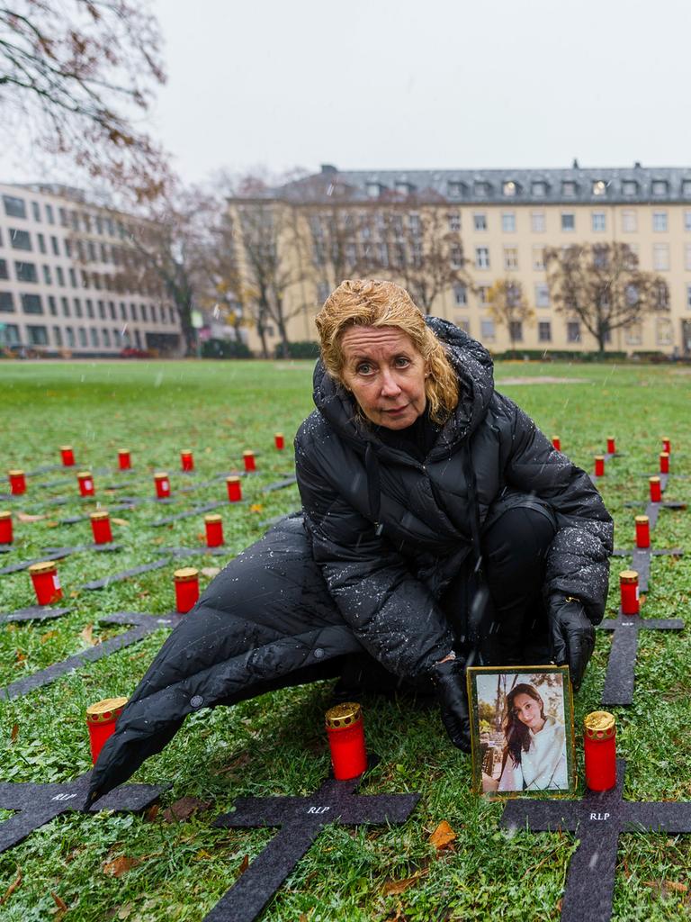 Inka Orth stellt auf einer Wiese, auf der mehrere schwarze Kreuze liegen, das Porträt ihrer verstorbenen Tochter Johanna neben eine Kerze ab.