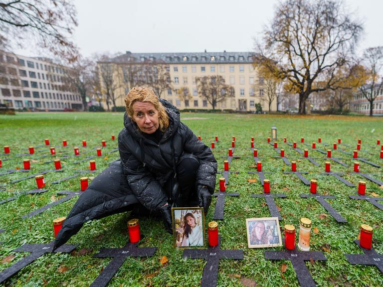 Inka Orth stellt auf einer Wiese, auf der mehrere schwarze Kreuze liegen, das Porträt ihrer verstorbenen Tochter Johanna neben eine Kerze ab.