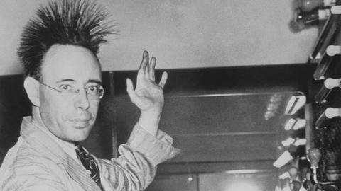 Eine Person lässt durch eine Kugel Elektrizität durch den Körper strömen. Dabei stellen sich die Haare auf. Das Foto stammt aus dem Jahr 1940 und ist in schwarz-weiß.