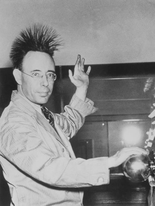 Eine Person lässt durch eine Kugel Elektrizität durch den Körper strömen. Dabei stellen sich die Haare auf. Das Foto stammt aus dem Jahr 1940 und ist in schwarz-weiß.