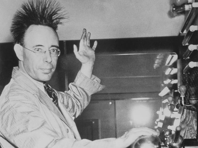 Eine Person lässt durch eine Kugel Elektrizität durch den Körper strömen. Dabei stellen sich die Haare auf. Das Foto stammt aus dem Jahr 1940 und ist in schwarz-weiß.
