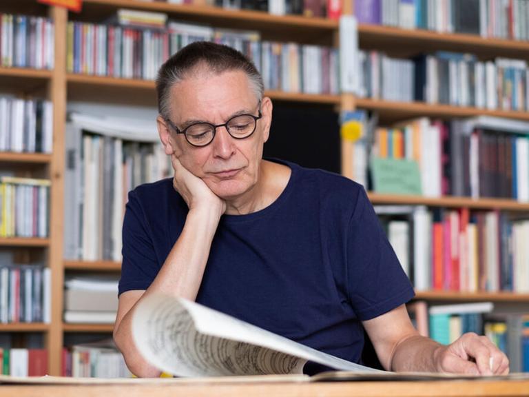 Ein Mann mit blauem T-Shirt sitzt in einer Bibliothek am Tisch und blättert in Noten