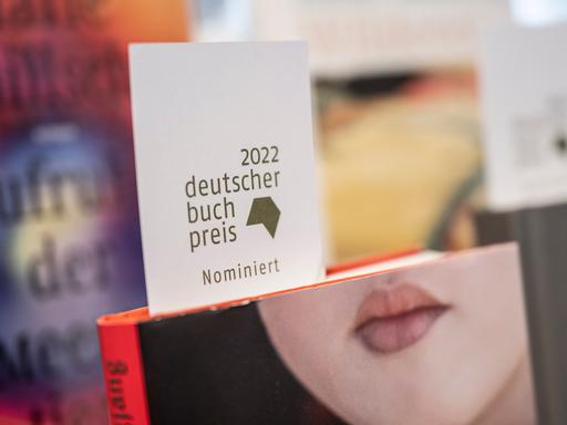 Ein Schild mit der Aufschrift "2022 deutscher Buchpreis nominiert" steckt in der Buchhandlung Bücher im Bogen in Frankfurt am Main in einem Buch mit einem Frauengesicht, bei dem nur der Mund zu sehen  ist.