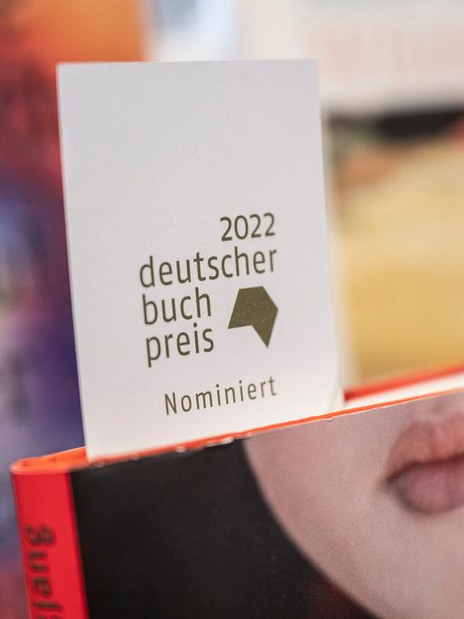 Ein Schild mit der Aufschrift "2022 deutscher Buchpreis nominiert" steckt in der Buchhandlung Bücher im Bogen in Frankfurt am Main in einem Buch mit einem Frauengesicht, bei dem nur der Mund zu sehen  ist.
